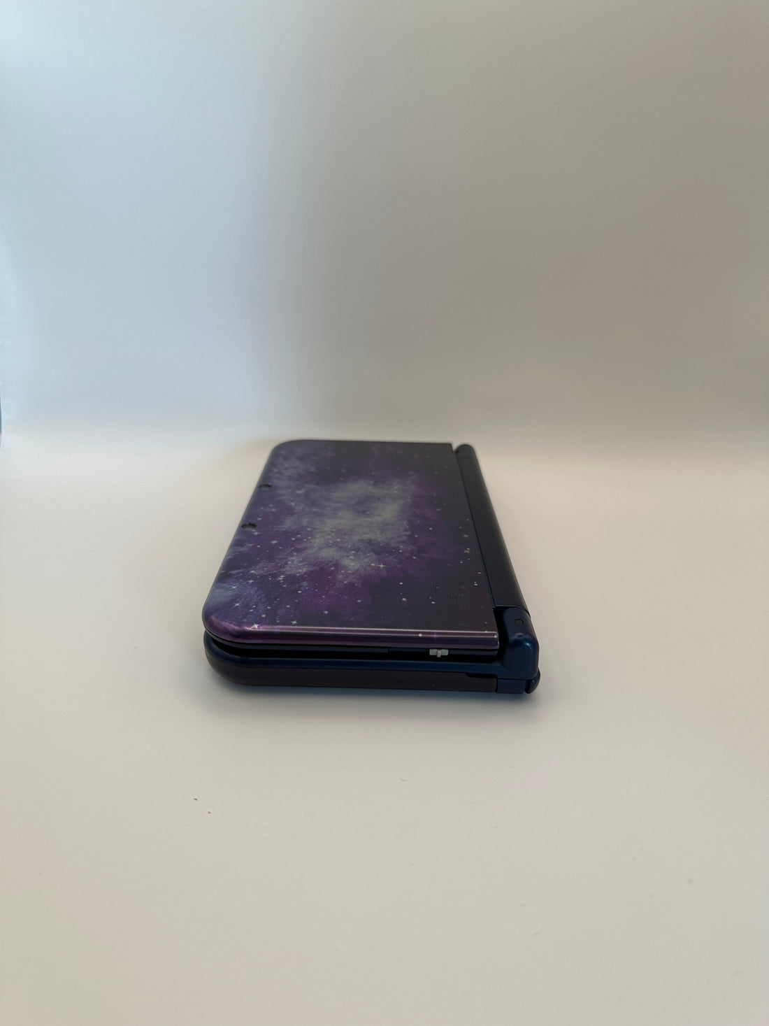 ReCollected New Nintendo 3DS XL handheld gaming console in a purple galaxy space pattern, closed side view.